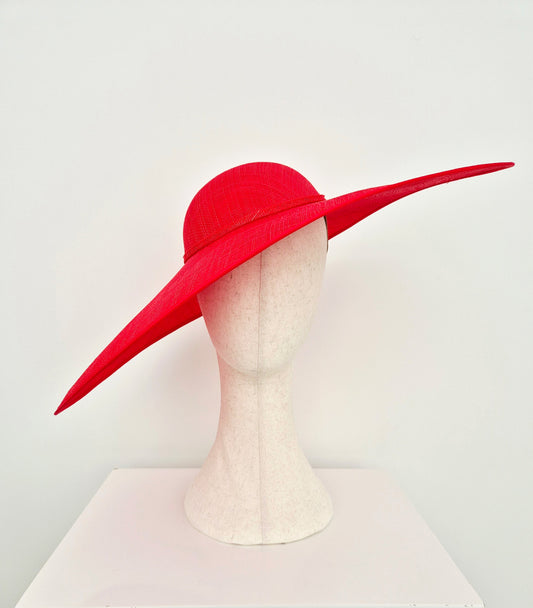 A bright red straw  wide-brimmed fascinator hat displayed on a white mannequin head against a plain white background.