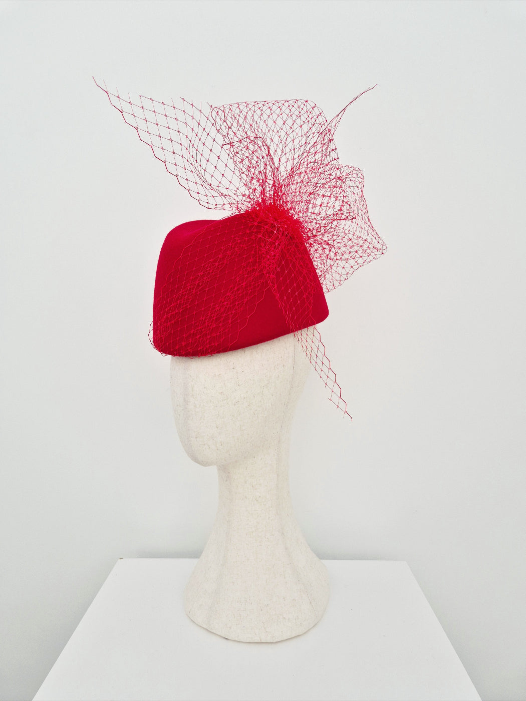 Red hat with a mesh veil on a mannequin head against a white background side view