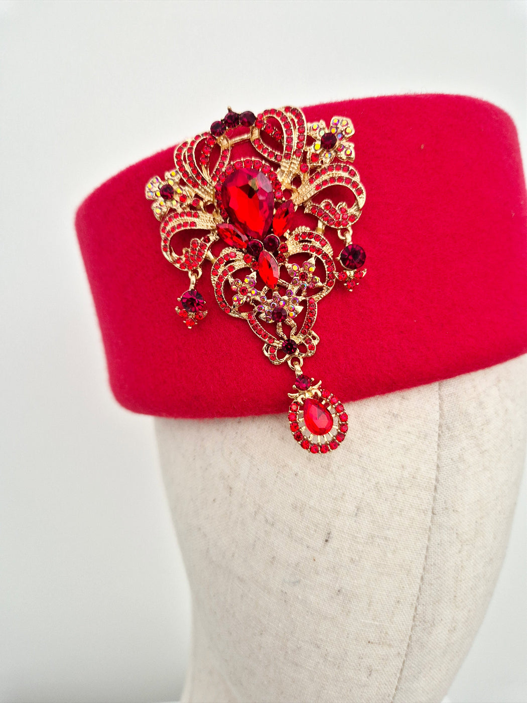 Red hat with a decorative brooch featuring gold and red gemstones on a mannequin head. close up