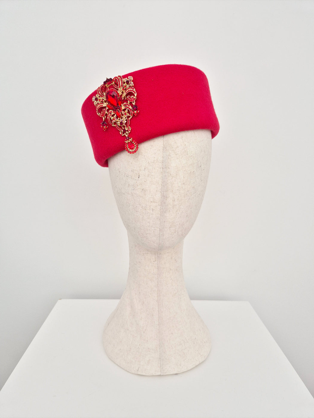 Red wool pillbox with gold embellishments on a mannequin head against a white background