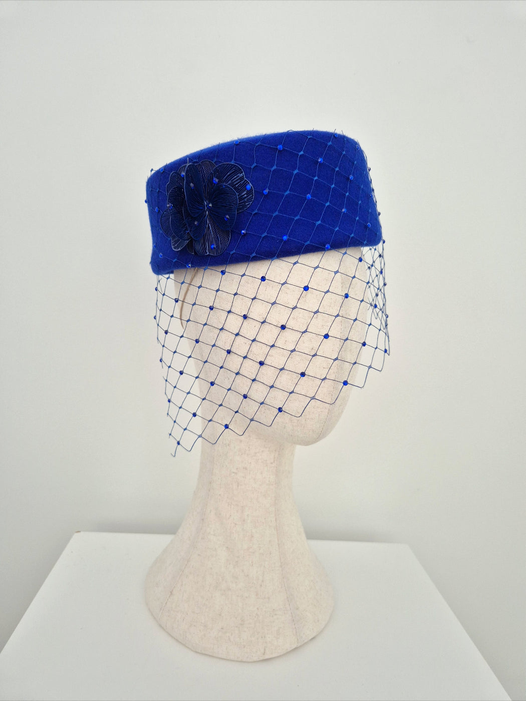 Blue pillbox hat with a net veil on a mannequin head against a white background side view