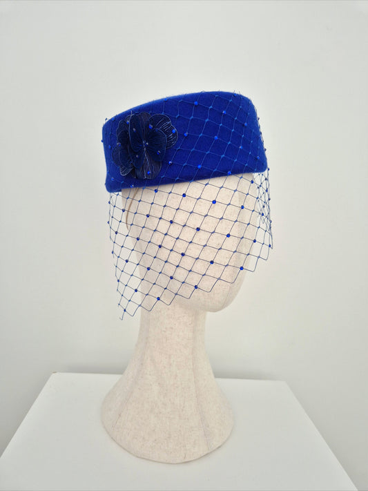 Blue pillbox hat with a net veil on a mannequin head against a white background side view