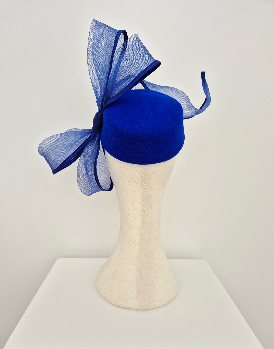 Blue felt pillbox fascinator with a large bow on a mannequin head against a white background back view