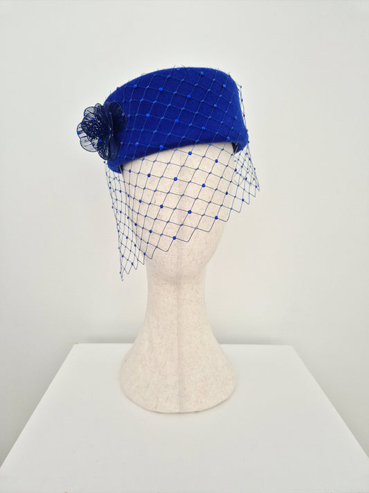 Blue pillbox headpiece with a netting veil on a mannequin head against a white background