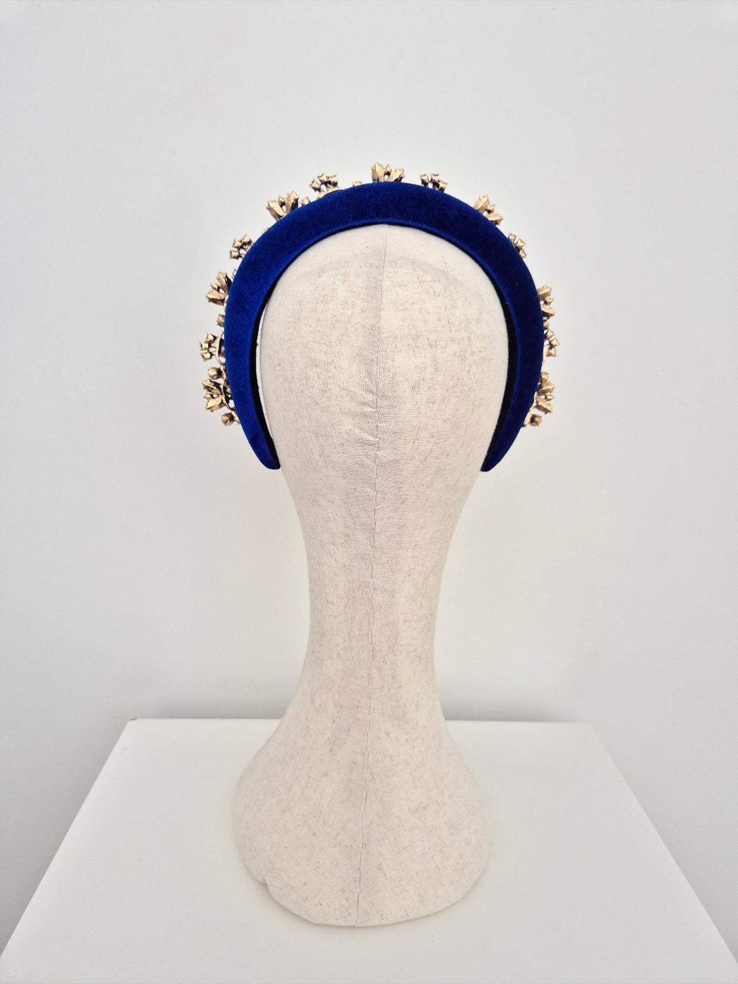 Royal blue headband with gold embellishments on a mannequin head against a white background back view