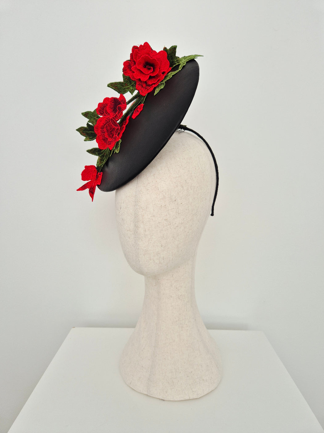 side front view of a black leather percher-plate headpiece with red lace detail on a manniquinn head 