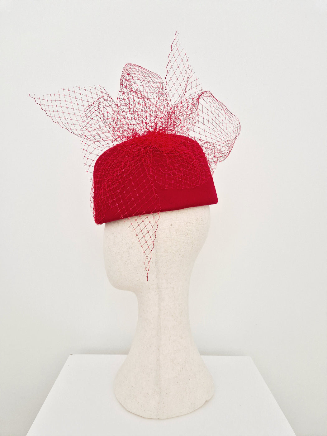 Red felt hat with a decorative mesh bow on a mannequin head against a white background side view 2