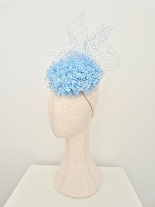 side view light blue 3d flower encrusted headpiece with veiling on a manniquin head against a white wall