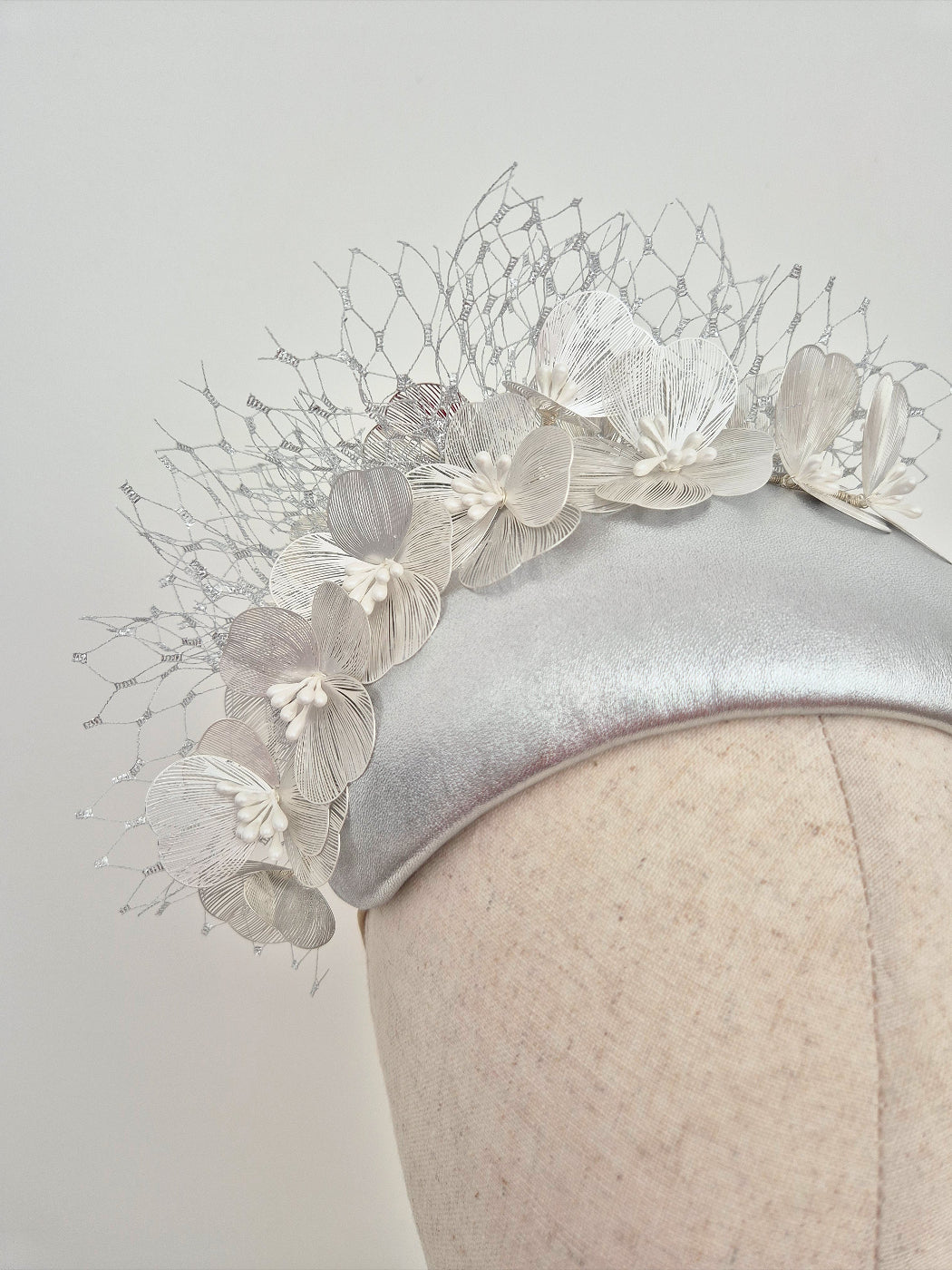 Silver headpiece with floral detail on a mannequin against a light gray background close up