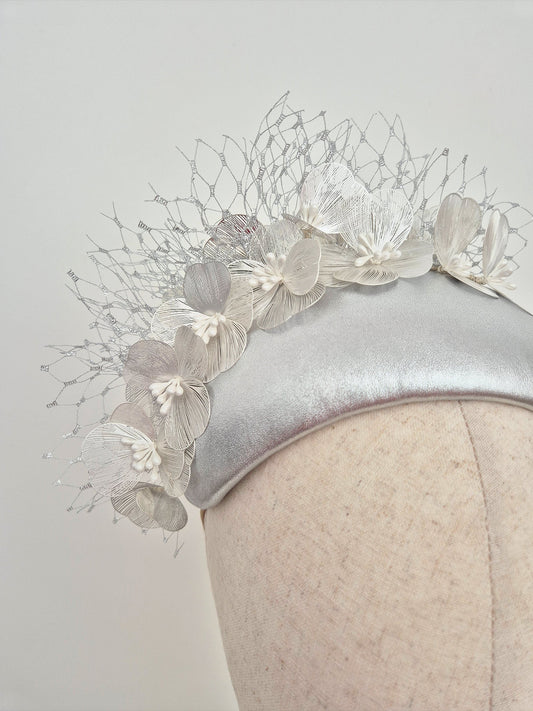 Silver headpiece with floral detail on a mannequin against a light gray background close up