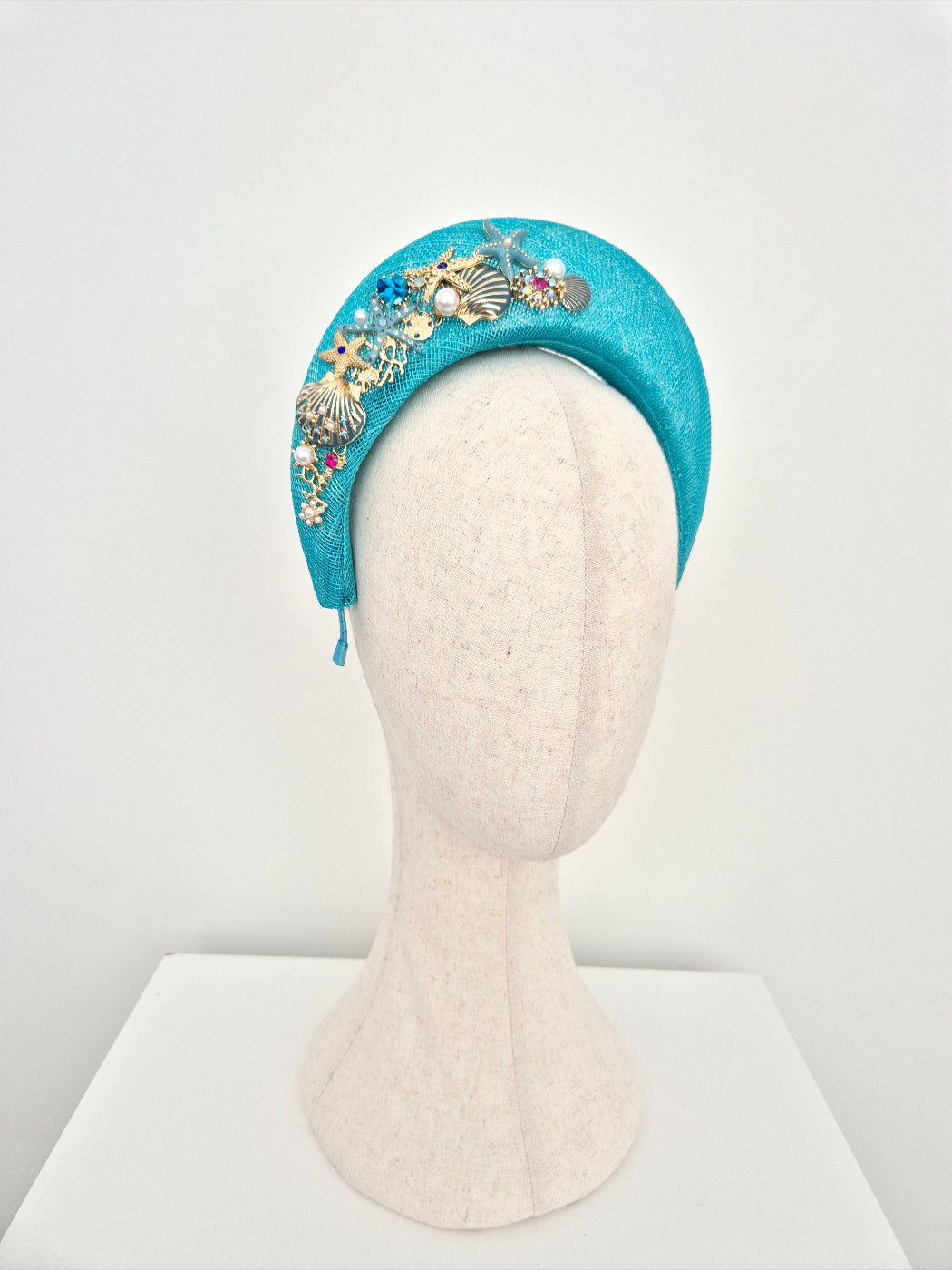 Turquoise headband with decorative elements on a mannequin head against a white background side view