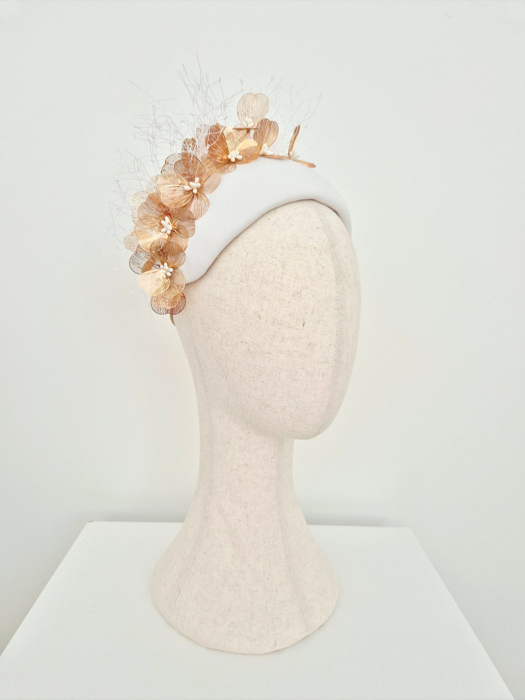 side front white leather headpiece with gold floral detail on a manniquin head against a white background