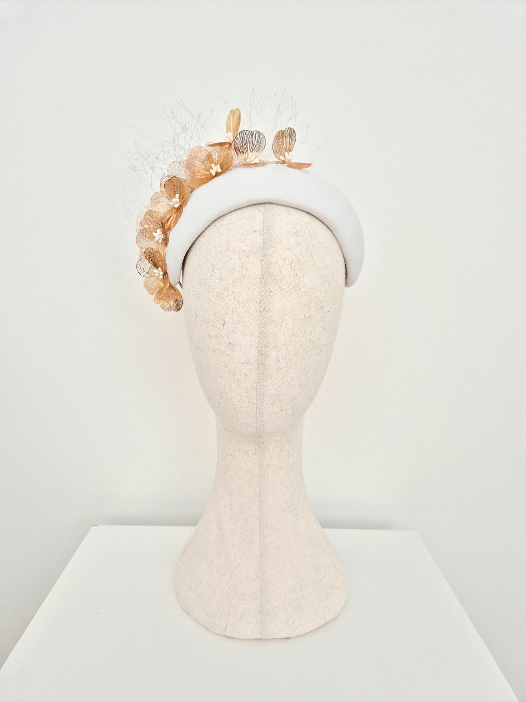 Mannequin head wearing a white leather headpiece with gold floral detail on a white background