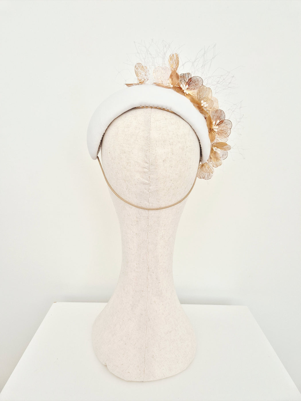 white headpiece with gold floral elements on a mannequin head against a white background back view