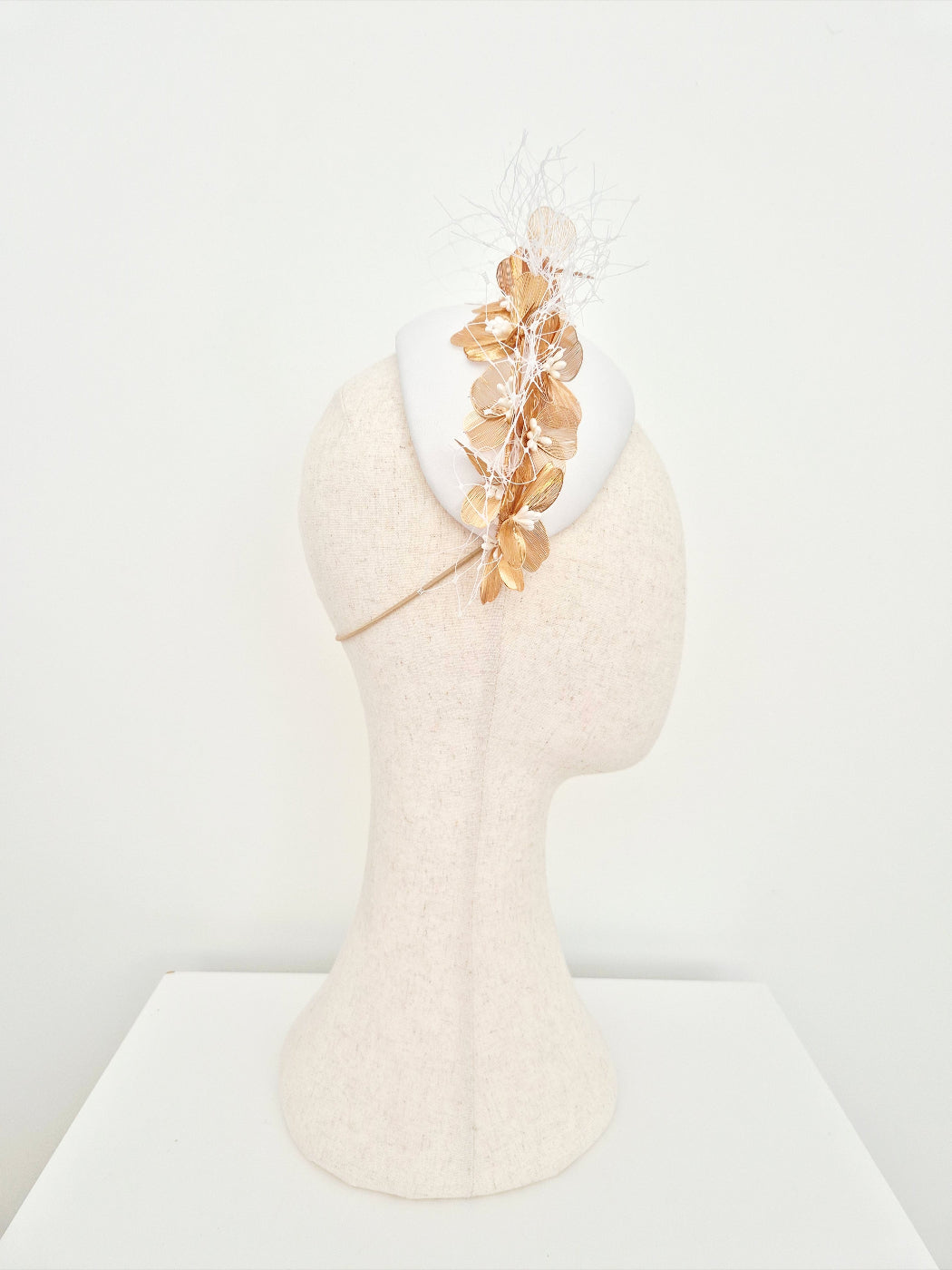 White headpiece with gold floral accents on a mannequin head against a white background back view