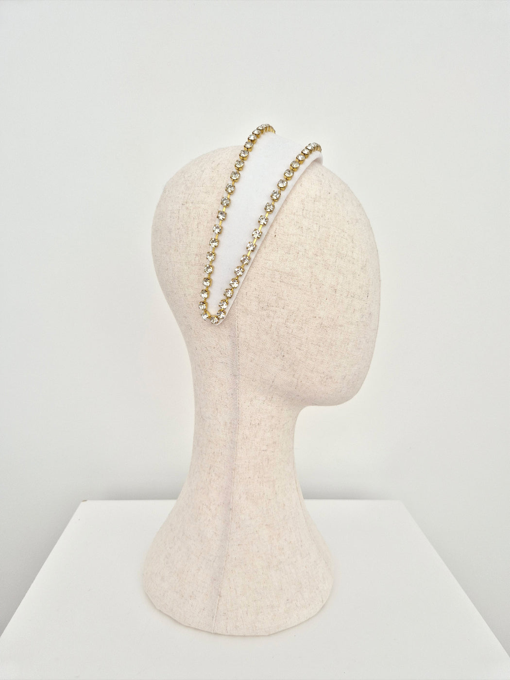 Mannequin head with white velvet headband with  gold set rhinestone trim on a white background side view