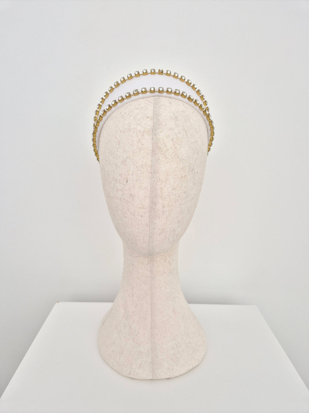 white velvet headband with gold set rhinestone trim on a mannequin head against a white background