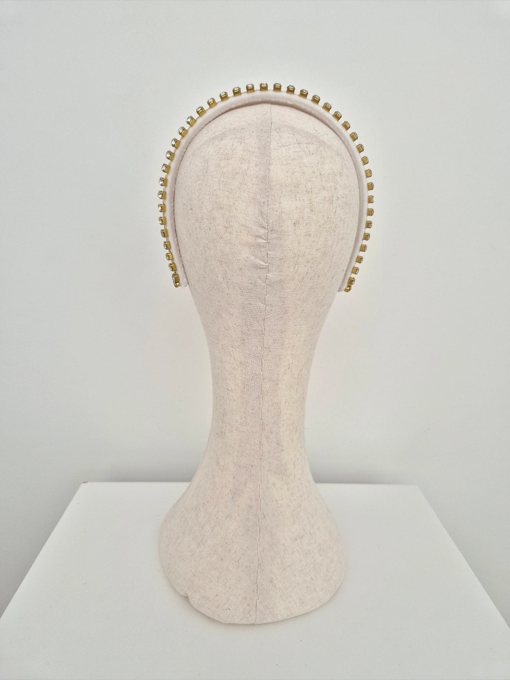 Mannequin head with white velvet headband with gold set rhinestone trim  on a white background back view