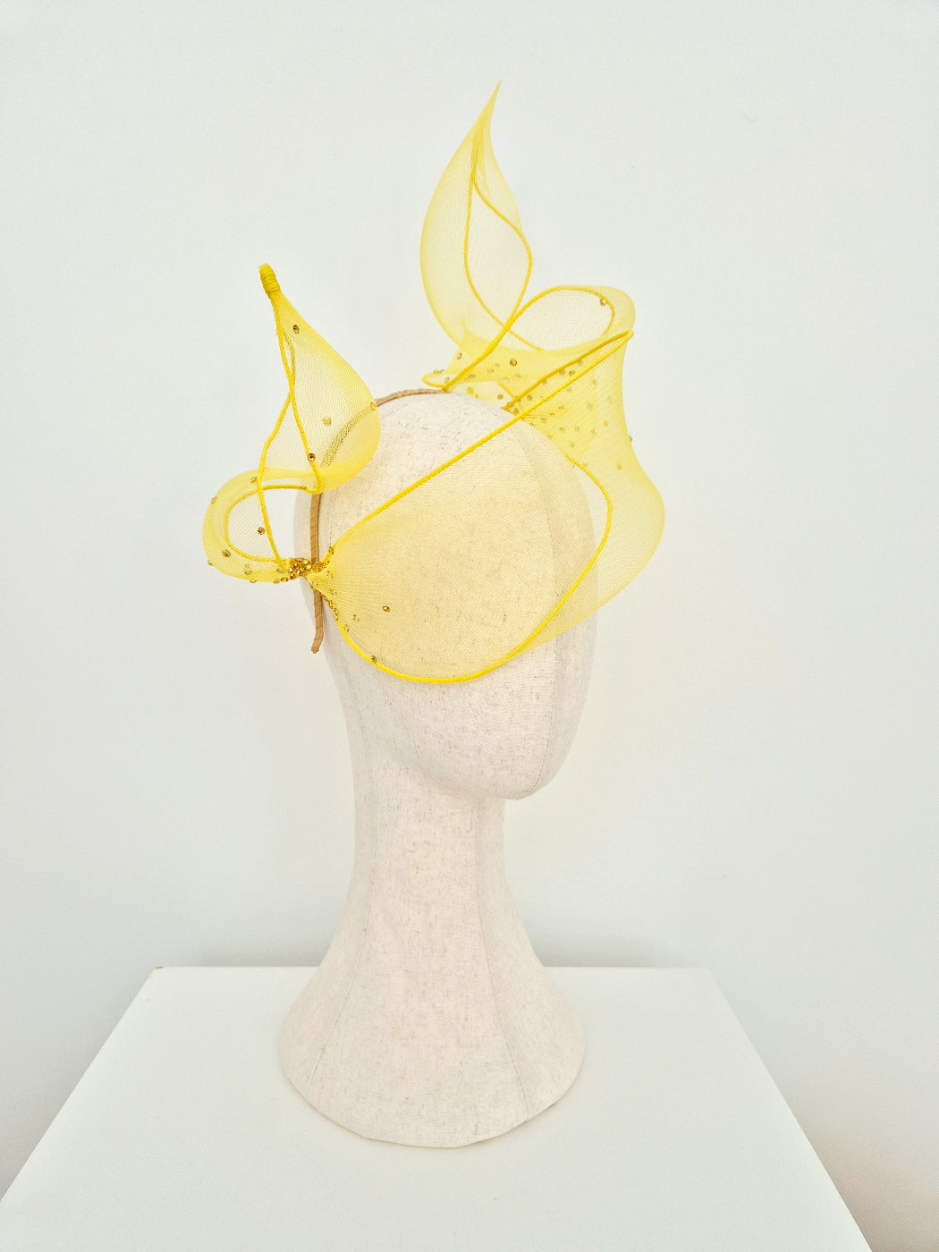 yellow crinoline fly away headpiece with scattered rhinestones on a manniquin head against a white background side view